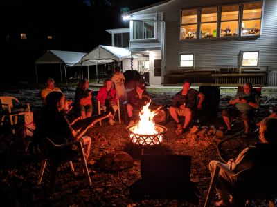 60th Anniversary Party Jack & Jan August 10, 2019
Campfire 6 
pic by Joe.  
Note the people in the Great Room, and the outside setup we had to accommodate everyone either indoors or outdoors.
L to R: Riley, toasting his "dogs: Jim; Joan; Grandma; Cole; Grandpa; Arik; John; others not in view (see other camp fire shots); Ann
