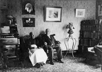 Joseph and Susanna Cheetham Higham at 418 Floyd Avenue. c1900
Joseph and Susanna Cheetham Higham seated in a room at 418 Floyd Avenue about 1900.  Note the lamp on the stand to the right of Joseph, the Smith-American Organ to the left of Susanna, and the Family Photo taken on the side lawn at the house about 1900.  The lamp and organ are in the possession of Jack & Jan Higham in Vestal, and viewable in the Ancestors Album.
